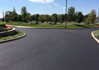 residential asphalt companies Freshly paved parking lot with new asphalt surrounded by trees, grass, and a few parked cars in the distance, almost like a paving gallery.