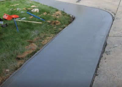 Freshly paved curved concrete sidewalk next to a grass lawn, with construction tools scattered beside it, resembling a scene straight out of a paving gallery.