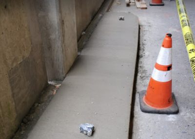 A freshly poured concrete curb stands next to an orange traffic cone and yellow caution tape, ready to become part of the paving gallery.