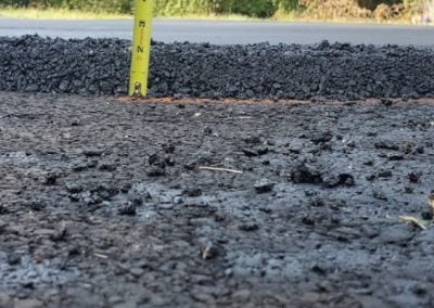 Close-up of a newly paved asphalt road, within a paving gallery, showing a measuring tape that indicates the depth of the asphalt layers.