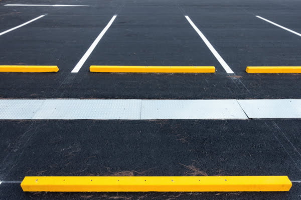 Empty parking lot with yellow wheel stops and white parking lines on freshly paved black asphalt. paving a parking lot